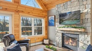Una sala de estar acogedora con chimenea de piedra, techo de madera y ventanas amplias.
