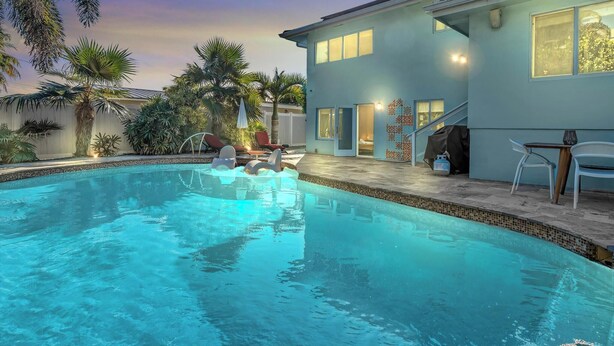 Une piscine avec des chaises longues, un patio couvert et une maison à la façade bleu clair.