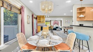 Un coin repas avec une table ronde dressée pour quatre personnes, entourée de chaises en osier avec des coussins orange.