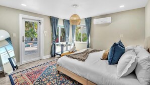 Une chambre avec un lit, un grand miroir, un tapis à motifs et une vue sur une piscine et la verdure environnante.