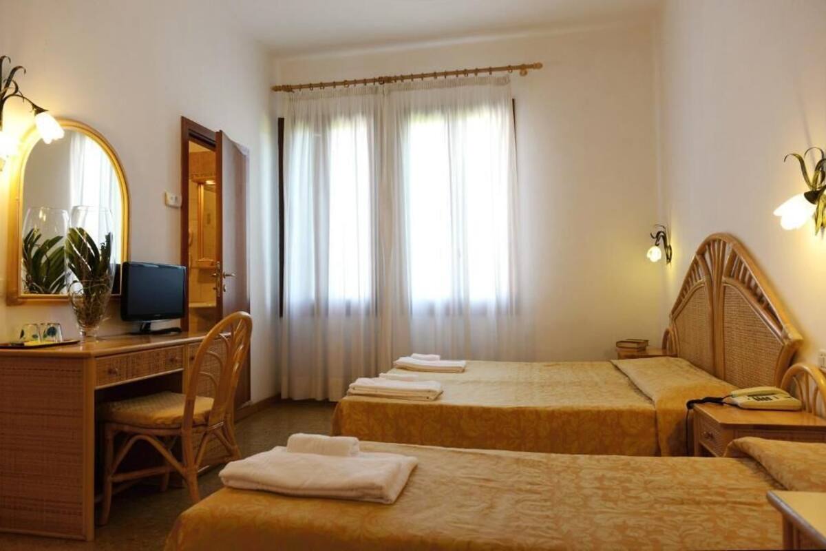 Ein Hotelzimmer mit zwei Betten, einem Schreibtisch mit Computer, einem Stuhl und einem Spiegel.