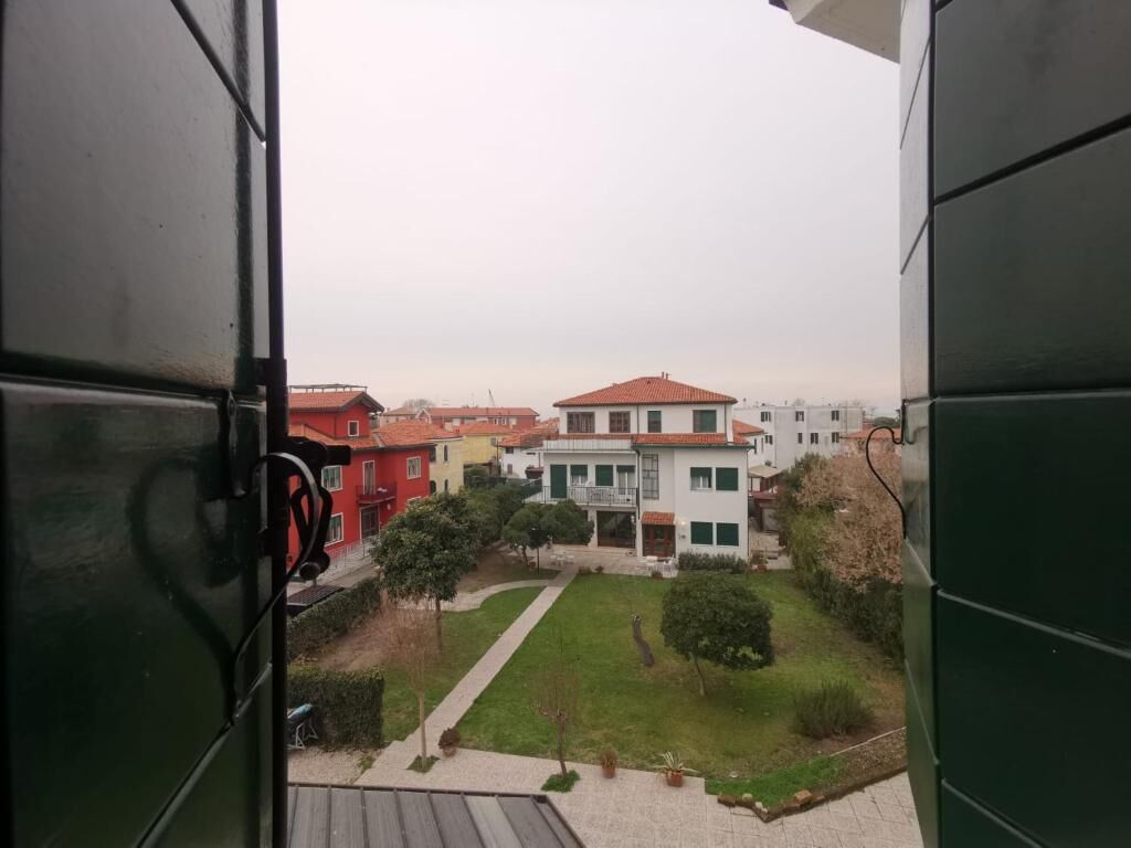 A view from inside a building looking out at a residential area with houses and a well-maintained lawn.