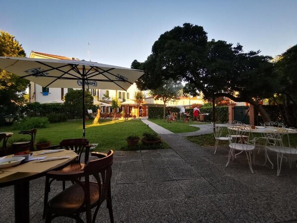An outdoor patio area with tables and chairs, a pathway, and a building in the background. - Hotel Orio (Venice)