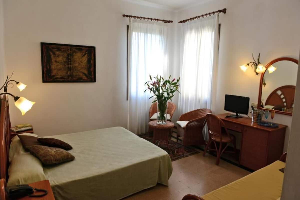 Ein Hotelzimmer mit Bett, Schreibtisch, Stuhl, Lampe und einem Bild an der Wand.