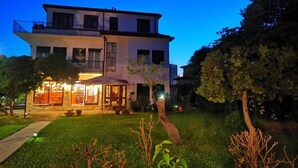A two-story building with a balcony, a covered outdoor seating area, and a well-maintained garden. - Hotel Orio (Venice)