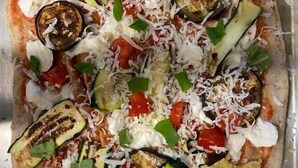 A pizza with various toppings including tomatoes, zucchini, and cheese on a tray. - Hotel Orio (Venice)
