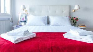 A hotel room with a large bed, white bedding, a red accent bedspread, two bedside tables with lamps, a framed picture, and a vase with flowers. - Hotel Orio (Venice)