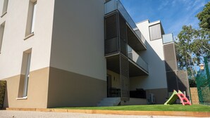 Un edificio moderno con techo plano, balcón y una pequeña zona de juegos con un tobogán.