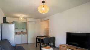 Una sala moderna con sofá, televisión, mesa de comedor con sillas, zona de cocina con refrigerador y lámpara colgante.