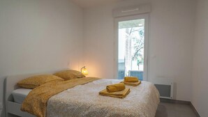 Un dormitorio con cama, lámpara de noche y ventana con vista a árboles.