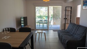 Una sala de estar con sofá, una mesa de comedor con sillas, televisor e iluminación colgante.