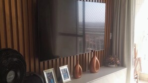 Un saló modern amb un gran televisor de pantalla plana muntat a una paret de fusta, un moble de televisió blanc a sota i un ventilador a l'esquerra.