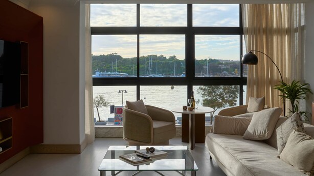 Un salon moderne doté d’une grande fenêtre donnant sur une marina, d’un canapé, d’une table basse en verre et d’un téléviseur placé à gauche.