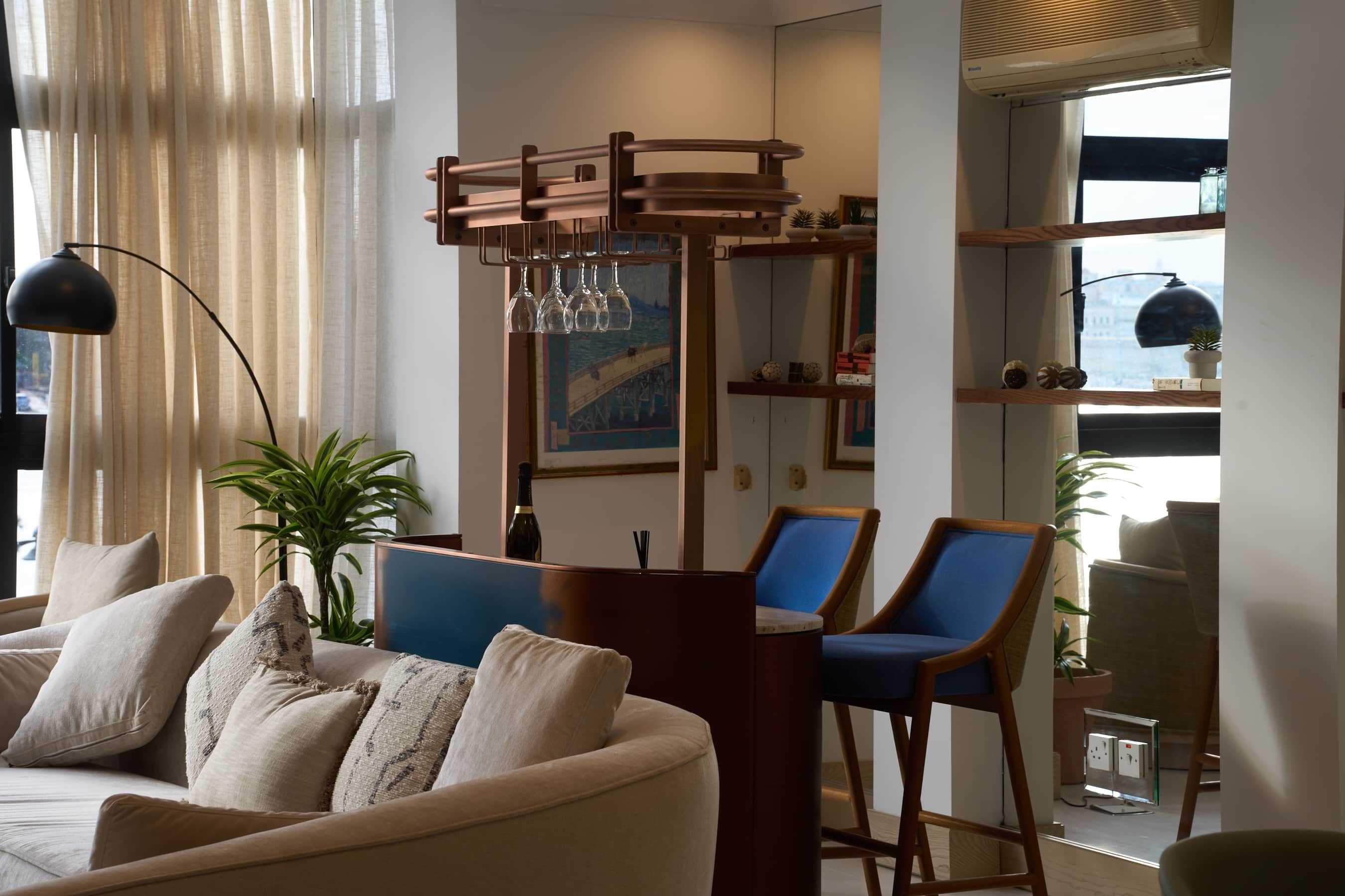 Un salon moderne comprenant un canapé, deux fauteuils bleus, une table basse en bois, une lampe sur pied et une bibliothèque agrémentée d’objets décoratifs.