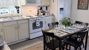 Una cocina con armarios blancos, microondas, estufa, refrigerador y una mesa de comedor con sillas.
