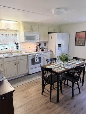 A kitchen with white cabinets, a microwave, stove, refrigerator, and a dining table with chairs.