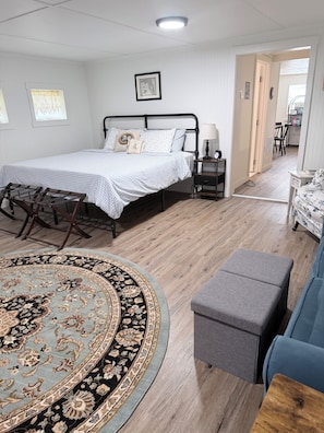 A bedroom with a bed, bedside table, lamp, and a view of the dining area.