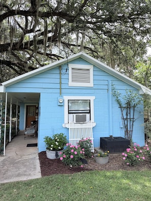 A blue house with a porch, a small window, and a white fence.