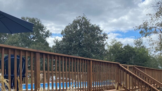 Una terraza de madera con una piscina al fondo.