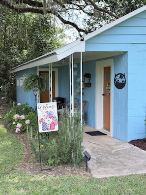 A blue house with a porch, a welcome sign, and a small garden.