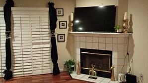 A living room with a fireplace, a flat-screen TV mounted above it, and a wooden floor. - Beautiful Gated 2-bedroom 1 bath Condo with fireplace in fabulous Hayward. (Hayward)