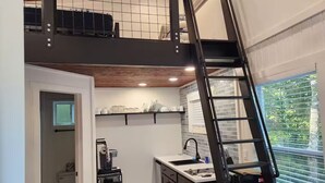 A modern kitchen with a black staircase, a coffee machine, and a window with blinds.