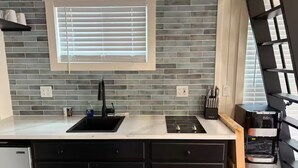 A modern kitchen with a black sink, a built-in stove, and a window with blinds.