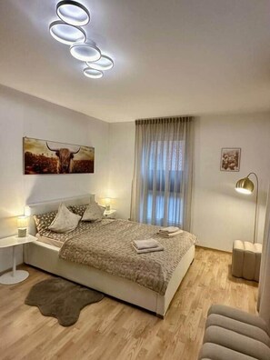 Un dormitorio con cama, mesitas de noche, lámpara de pie, alfombra, ventana con cortinas y una obra de arte colgada en la pared.