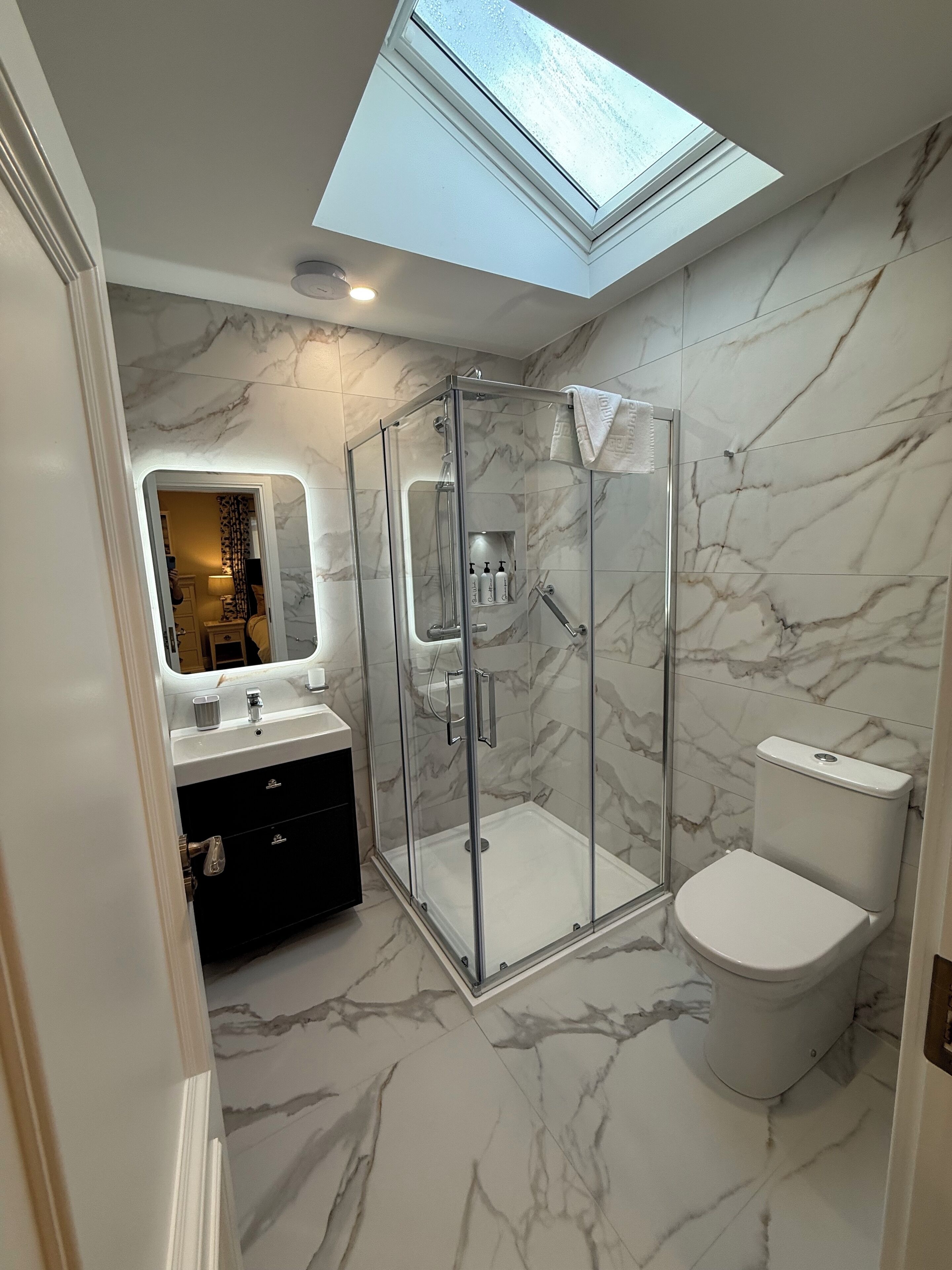 A modern bathroom with a skylight, a glass-enclosed shower, a toilet, and a vanity with a mirror.