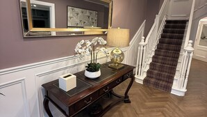 Un pasillo con un aparador de madera oscura, un espejo grande y una escalera con alfombra escocesa.