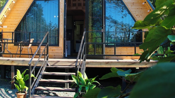 Een houten chalet met een puntig dak, grote ramen en een houten terras.