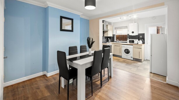 A modern kitchen with a dining area, featuring a central island, built-in appliances, and a light blue accent wall. - Contractor 3-Bed Long-Stay & Discounts  (Reading)