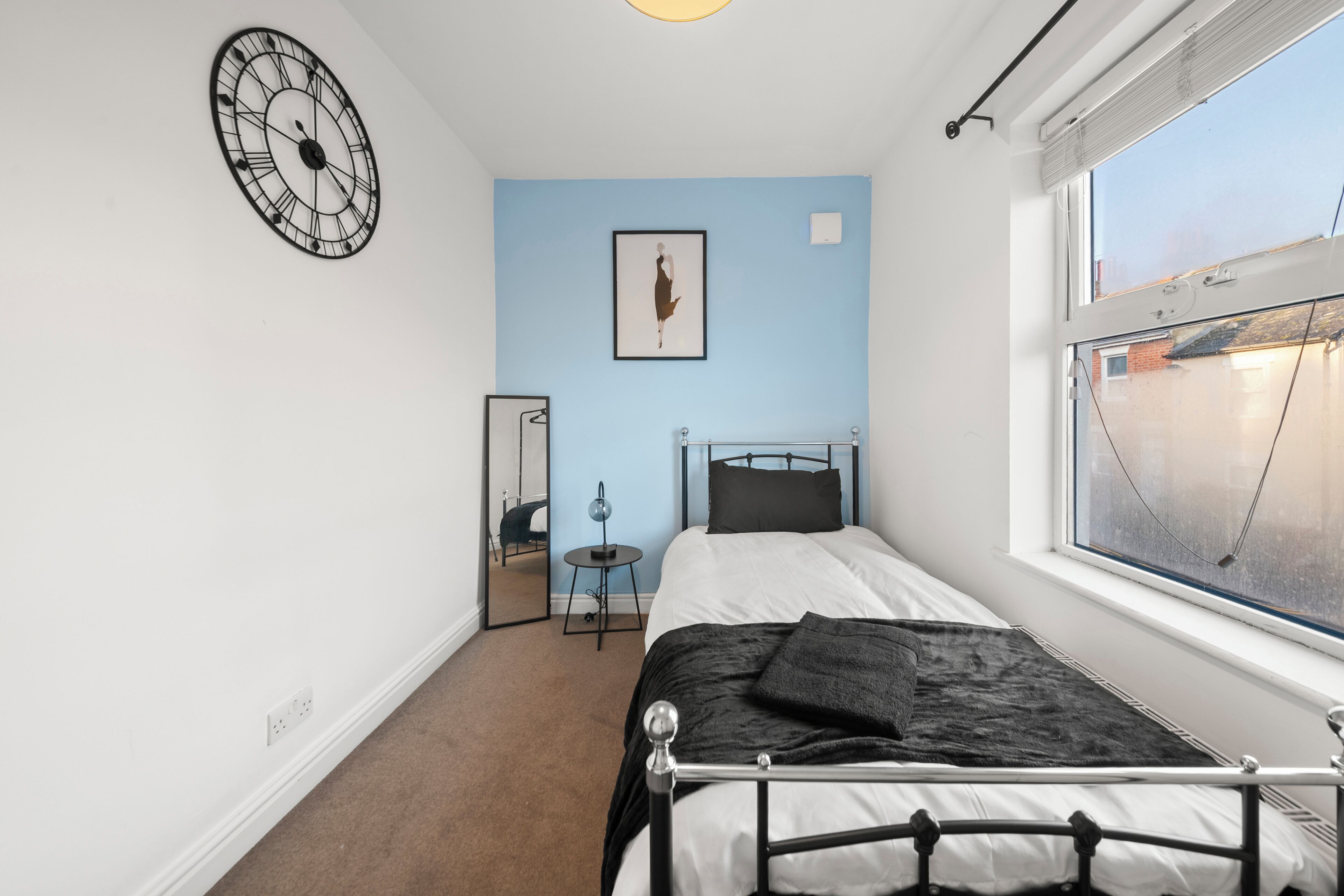 Un dormitorio con cama, un reloj en la pared, una ventana y un espejo.