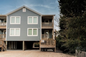 Charming coastal cottage elevated on stilts, featuring multiple levels of deck space and covered parking beneath for beach gear storage.