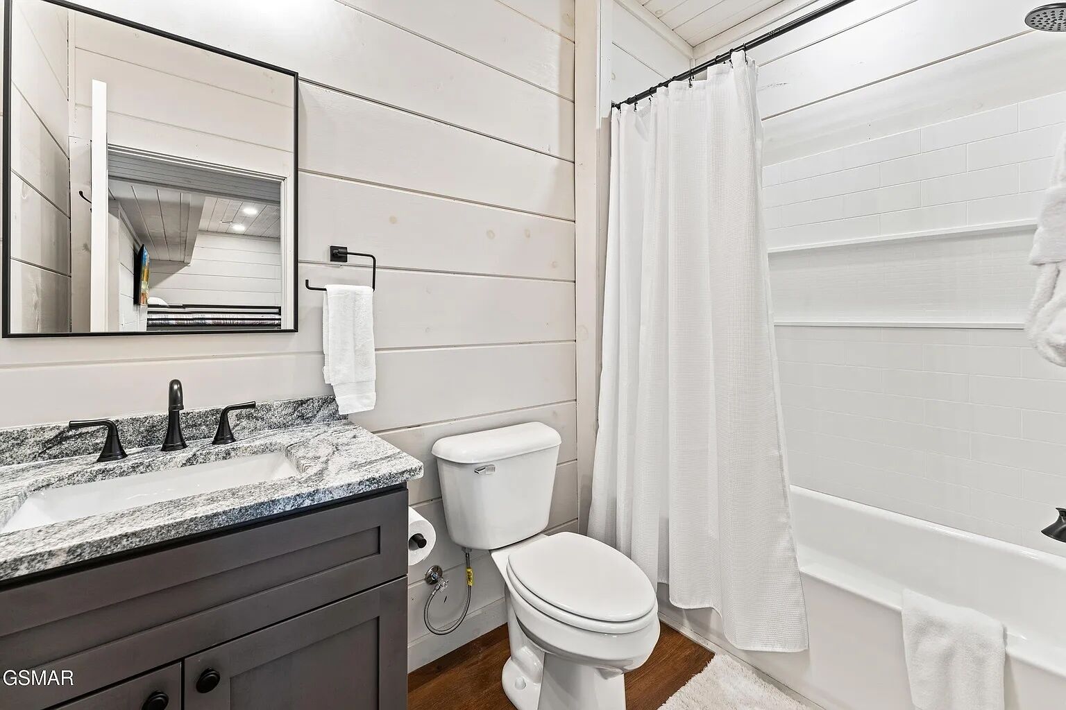Ein Badezimmer mit einer weißen Toilette, einem Waschbecken mit einer Granitplatte, einem Spiegel und einer Duschvorhang.