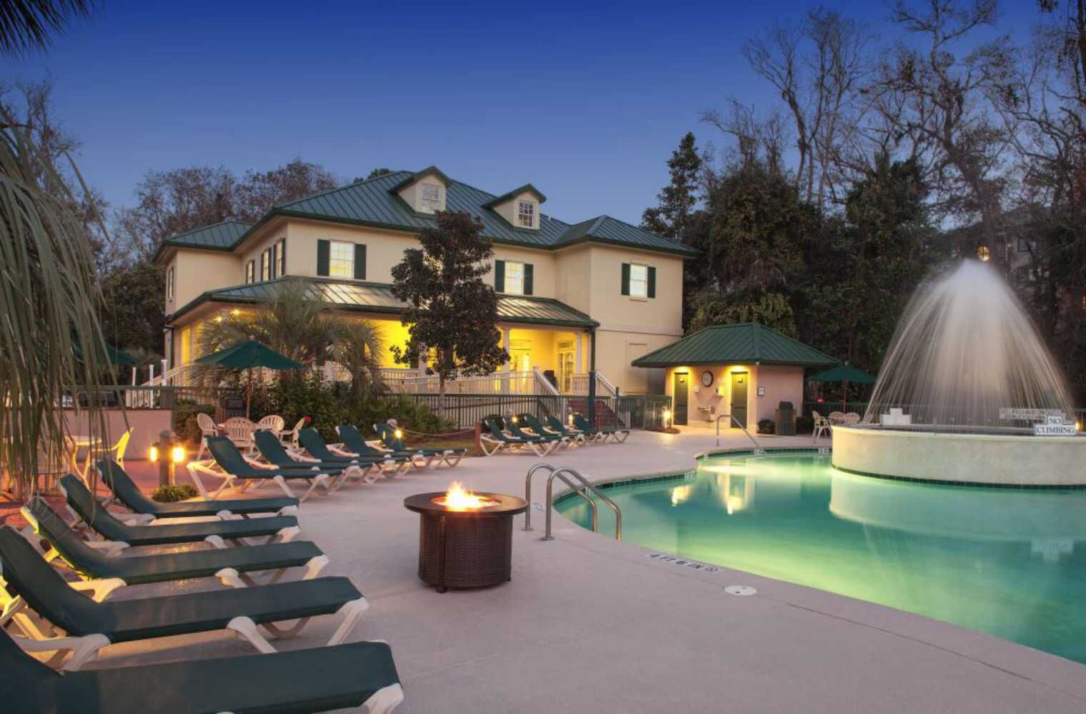 Un área junto a la piscina con sillones de descanso, una chimenea y una fuente.