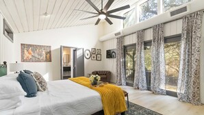 Ein Schlafzimmer mit einem großen Bett, einem Deckenventilator, einem Fenster mit Vorhängen und einer Tür.