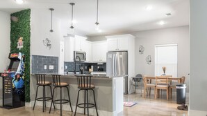 A modern kitchen with white cabinets, a stainless steel refrigerator, and a bar area with stools. - Modern Lake Escape Arcade EV Fun (Denison)