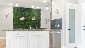 A modern kitchen with a green wall backsplash, white cabinets, stainless steel dishwasher, and pendant lighting. - Modern Lake Escape Arcade EV Fun (Denison)