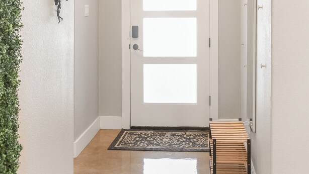 A hallway with a white door, a small bench, a patterned rug, and a wall-mounted light fixture. - Modern Lake Escape Arcade EV Fun (Denison)