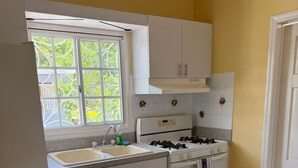 Una cocina con gabinetes blancos, una estufa a gas, un fregadero y una ventana con vista a la vegetación.