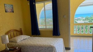 Una habitación con dos camas, una ventana con cortinas, una mesita de noche y vista al mar a través de un arco.