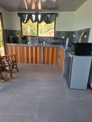 A kitchen with a wooden countertop, a refrigerator, and a window with curtains.