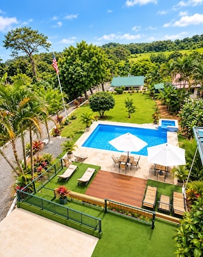 A swimming pool with a patio area, surrounded by lush greenery and a view of a hilly landscape.
