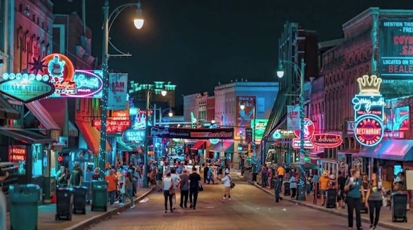 Una calle concurrida bordeada de letreros de neón brillantes y escaparates, lo que denota una zona urbana vibrante.