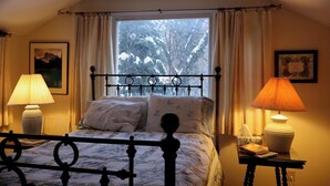 Ein Schlafzimmer mit einem Bett, zwei Nachttischlampen, einem Fenster mit Vorhängen und einem gerahmten Bild an der Wand.