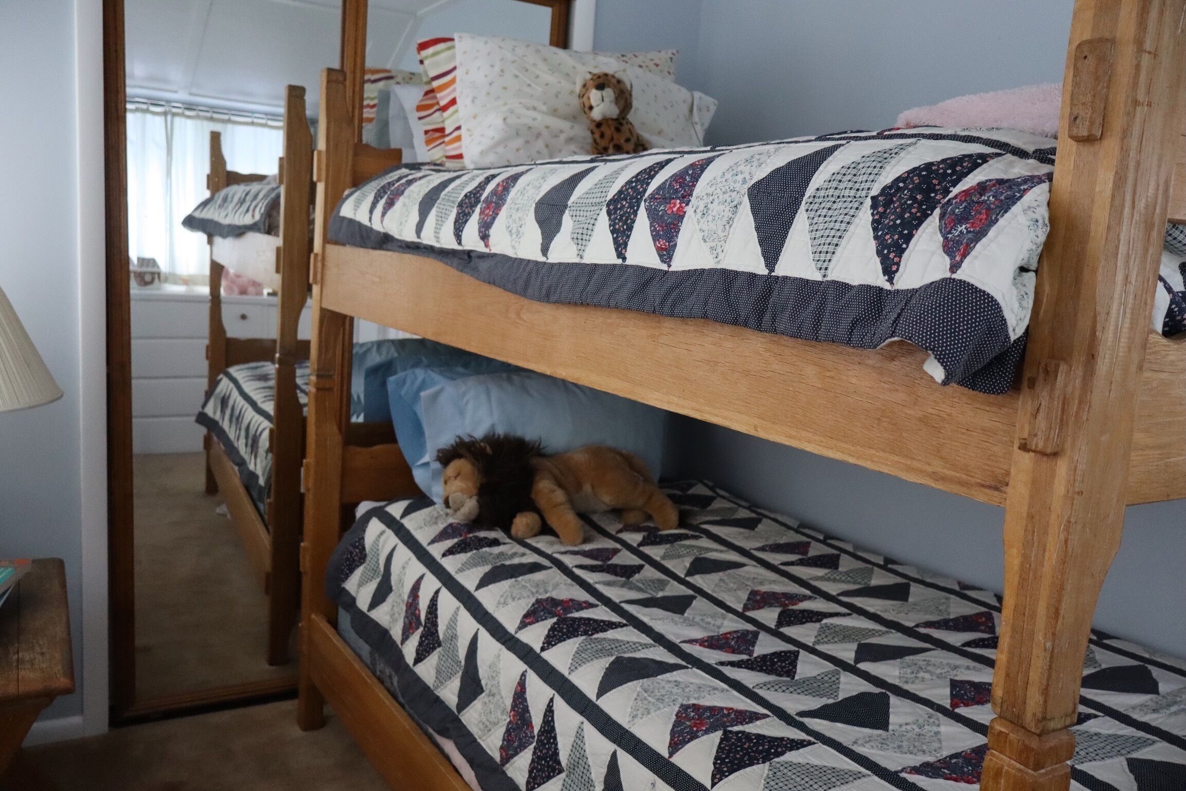 Een stapelbed met een geborduurde sprei, een pluche speelgoed en een houten hoofdbord.