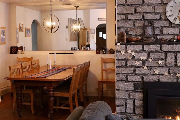 A dining area with a wooden table and chairs, a chandelier, and a brick fireplace with star decorations.