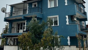 Többszintes lakóépület, amelynek erkélyei, műholdas antenna és kerítéssel ellátott udvara van.