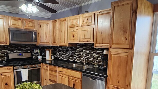 Una cocina con armarios de madera, encimera negra, ventilador de techo e iluminación colgante.